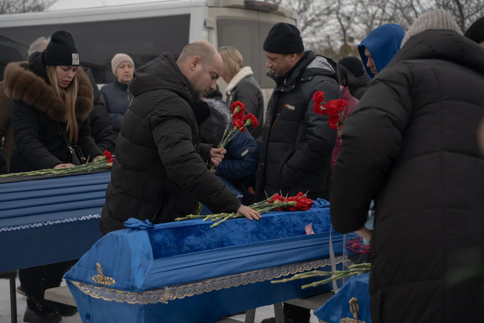 Мужчина кладет цветы на гроб. Вокруг толпа.